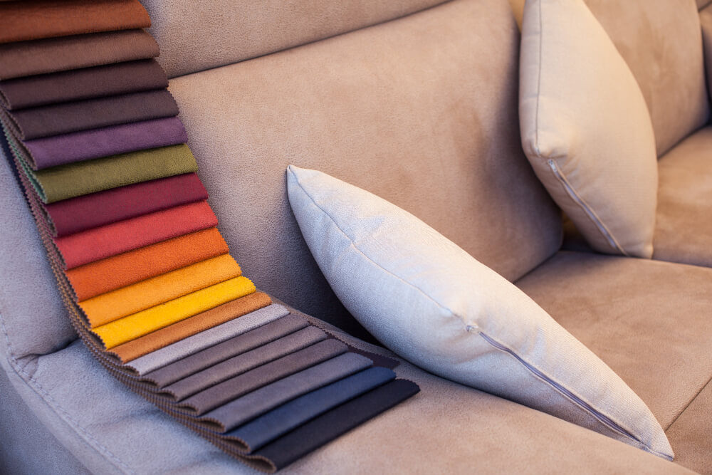 A cozy couch adorned with colorful pillows and a neatly arranged stack of vibrant fabric.